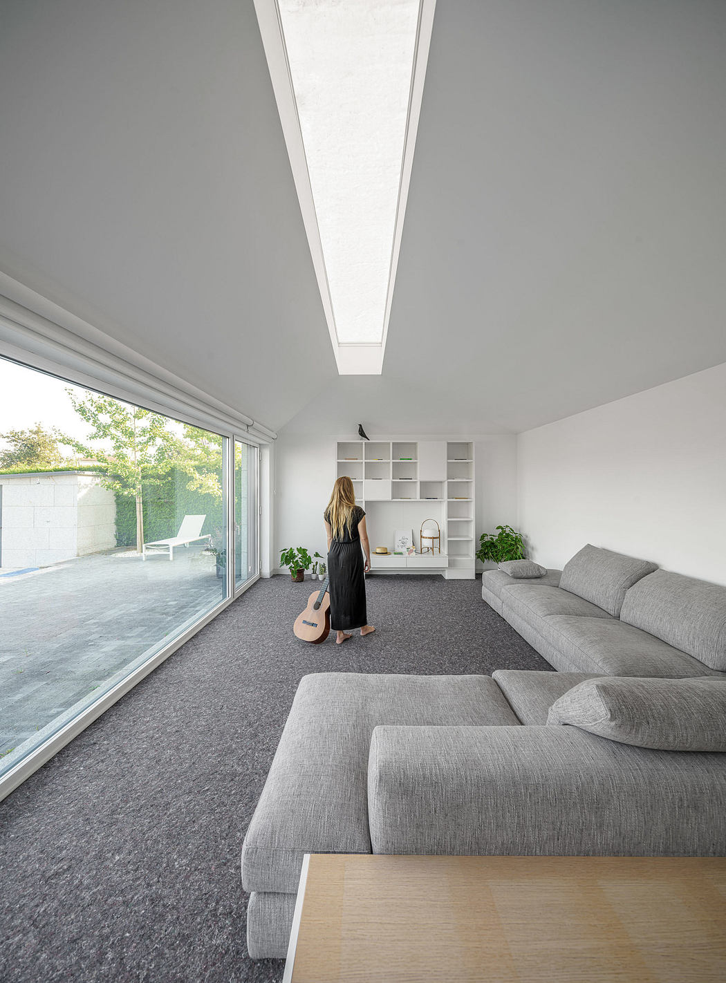 A woman in a minimalistic living room with large windows and modern sofa.
