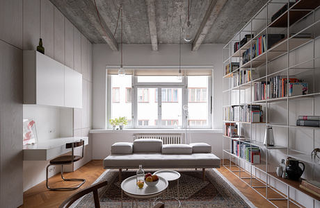 Modern living room with exposed concrete ceiling and bookshelf wall.