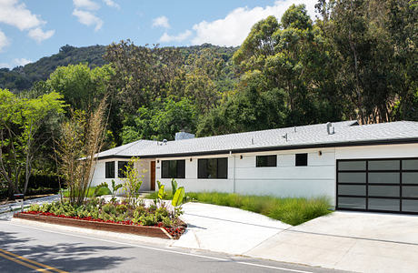 Modern single-story house with a white facade and landscaped driveway against a hillside