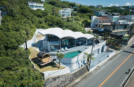 Modern house with curved roof, pool, and large windows overlooking a street.