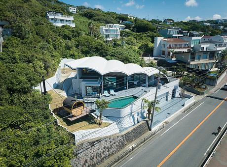 Modern house with curved roof, pool, and large windows overlooking a street.