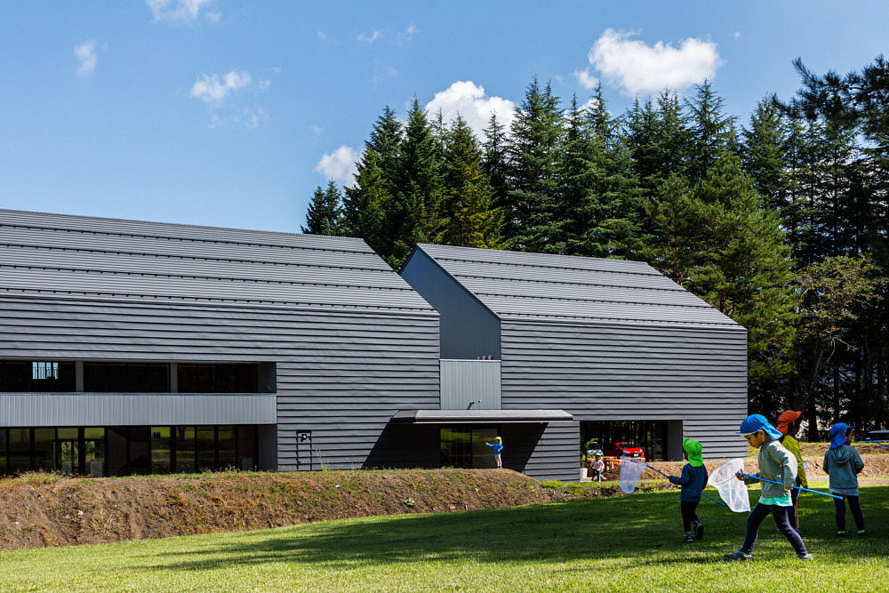 Modern building with a sloped roof against a backdrop of trees, with children playing