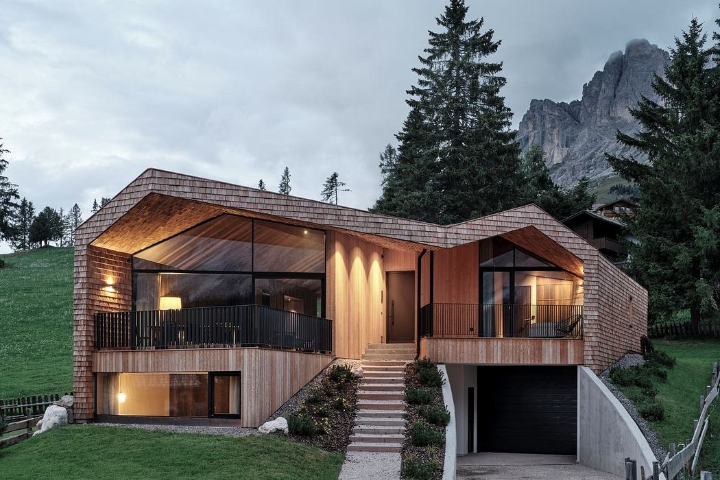 Modern wooden house with large windows nestled in a mountainous area.