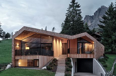 Modern wooden house with large windows nestled in a mountainous area.