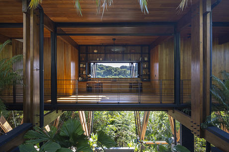 Wooden interior of a tropical home with large windows overlooking greenery.