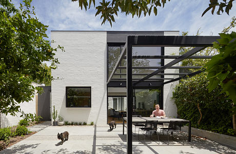 Modern backyard with a white brick house, patio furniture, and a pergola.