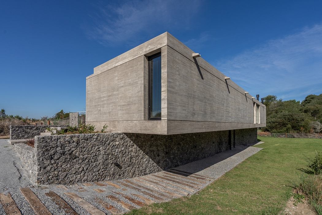 Modern concrete house with large windows on a stone base.