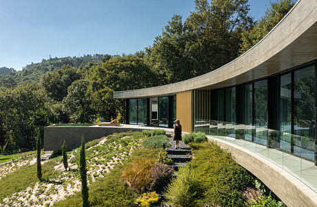 Modern curved house with large windows and a green roof garden.