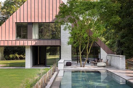 Modern two-story house with a pool and large windows, surrounded by trees.