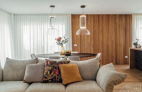 Modern living room with a beige sofa, wooden wall paneling, and pendant lights