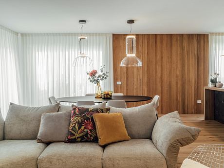 Modern living room with a beige sofa, wooden wall paneling, and pendant lights