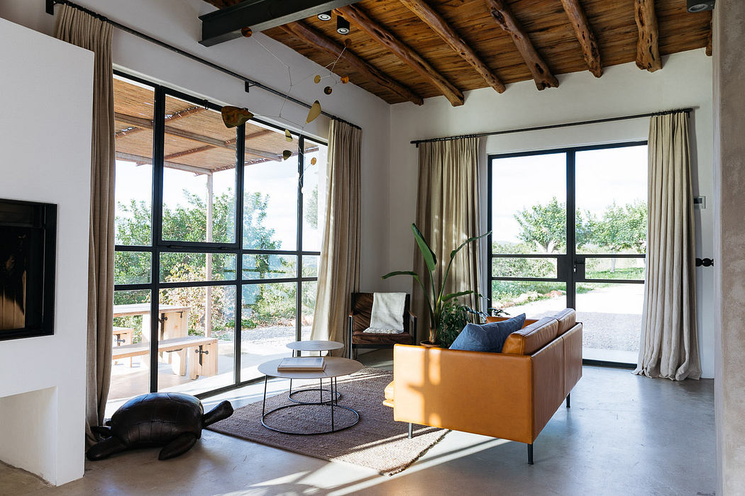 Modern living room with large windows, a tan sofa, and wooden ceiling beams.
