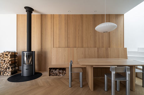 Modern minimalist dining area with wood paneling and a freestanding fireplace.