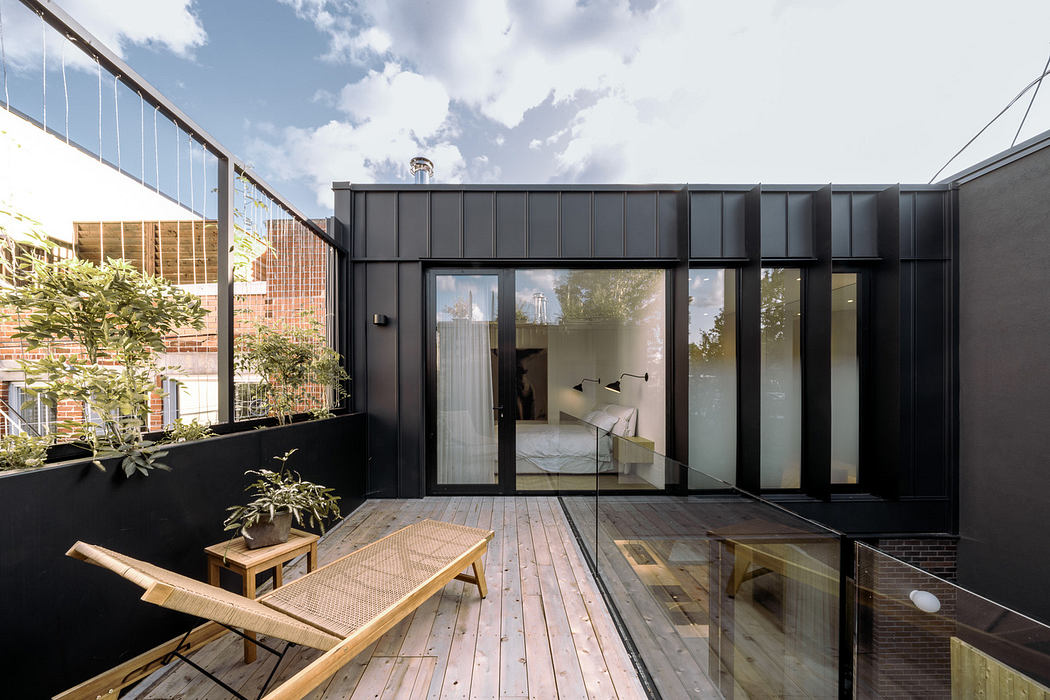 Modern terrace with wooden decking and black facade, featuring large glass doors.