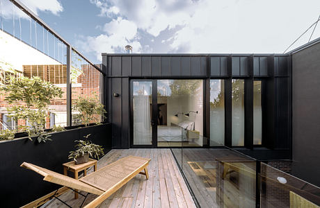 Modern terrace with wooden decking and black facade, featuring large glass doors.