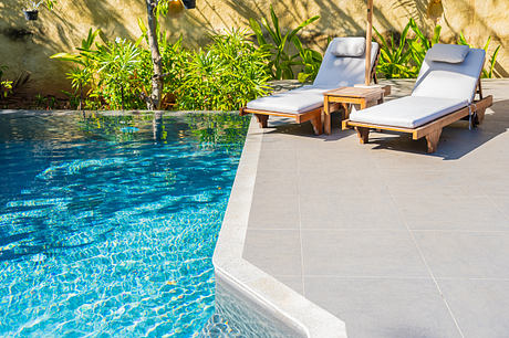 Two sun loungers beside a tranquil pool with tropical foliage.