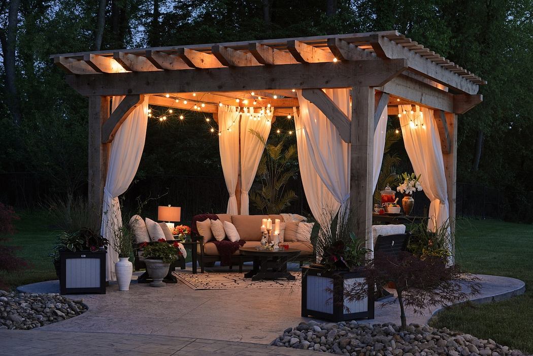 Cozy garden pergola with lights and draped curtains at dusk.