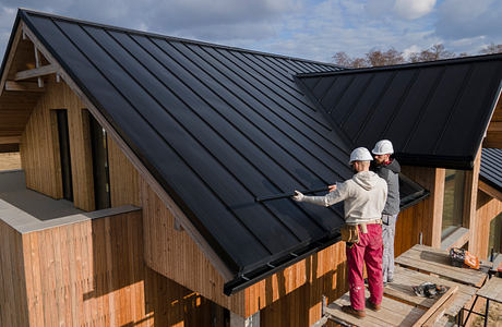 Workers on a roof of a modern house with wooden siding.