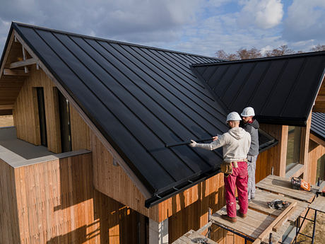 Workers on a roof of a modern house with wooden siding.