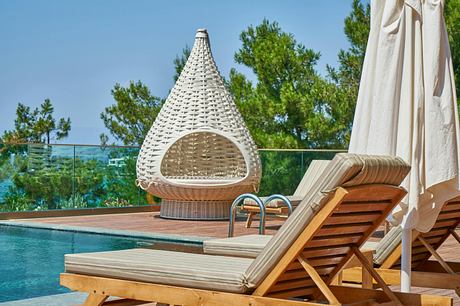 Poolside lounge area with modern chairs and a unique wicker canopy seat.