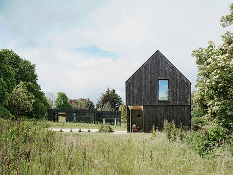 Contemporary pitch-roofed black timber houses amid lush greenery.