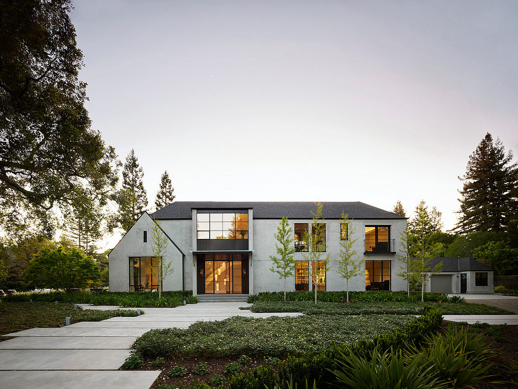 Modern two-story house with large windows, surrounded by trees at dusk.