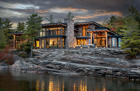 Contemporary lakeside house with expansive windows and stone details at dusk.