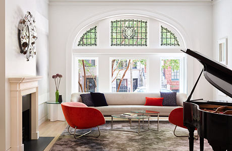 Elegant living room with grand piano, red chairs, and arched windows.