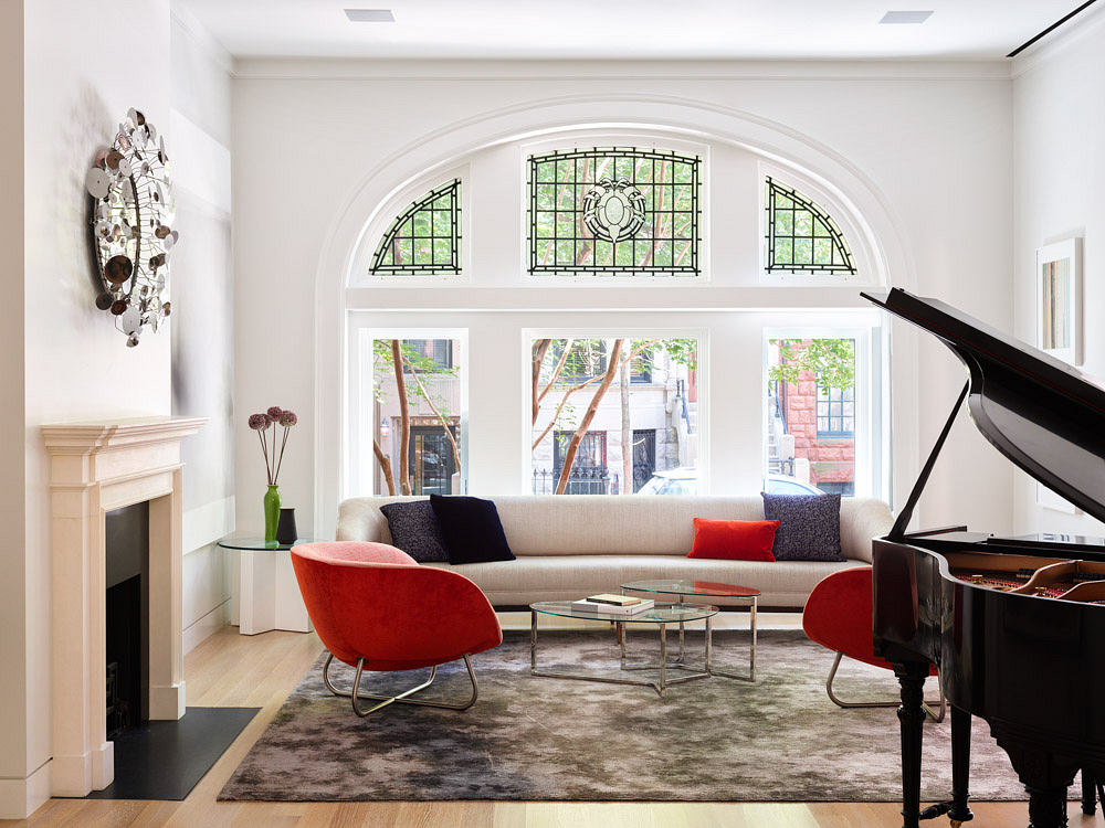 Elegant living room with grand piano, red chairs, and arched windows.