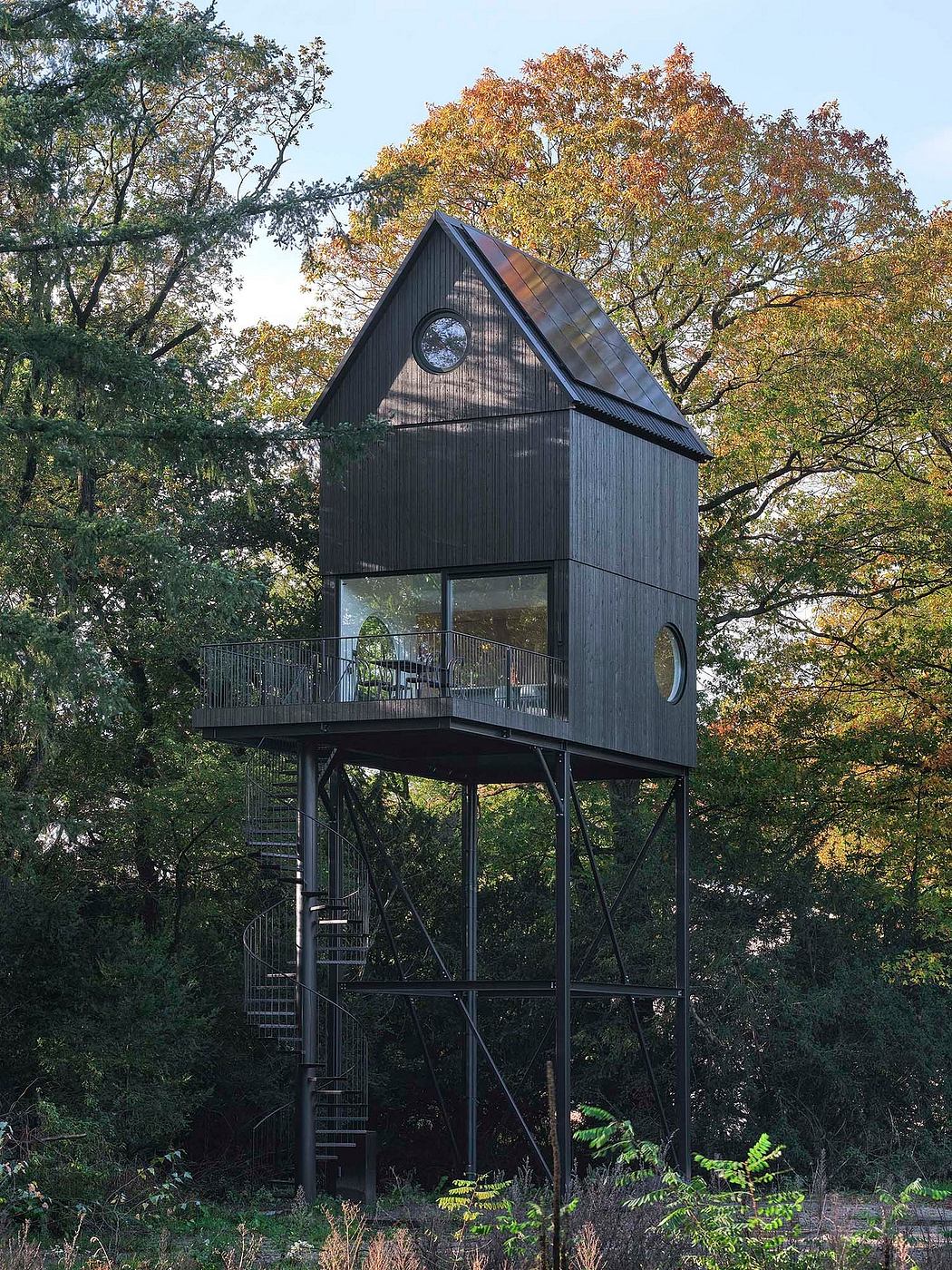 Elevated, slender cabin with a gabled roof amid trees.