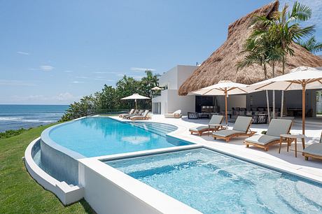 Luxurious seaside infinity pool with thatched pavilion and lounge chairs.