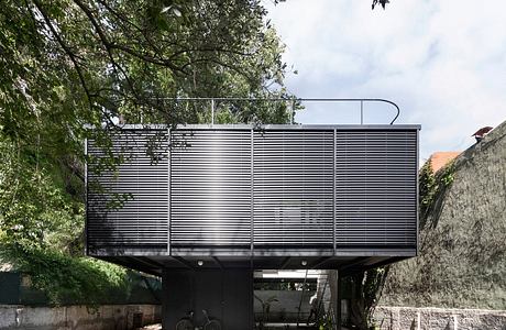 Contemporary house with metal facade elevated above a pool and terrace area, surrounded by