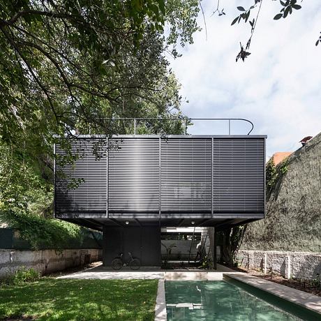 Contemporary house with metal facade elevated above a pool and terrace area, surrounded by