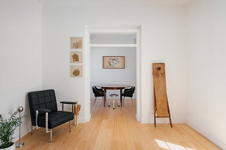 Minimalist interior with a black chair, wooden floor, and a peek into an