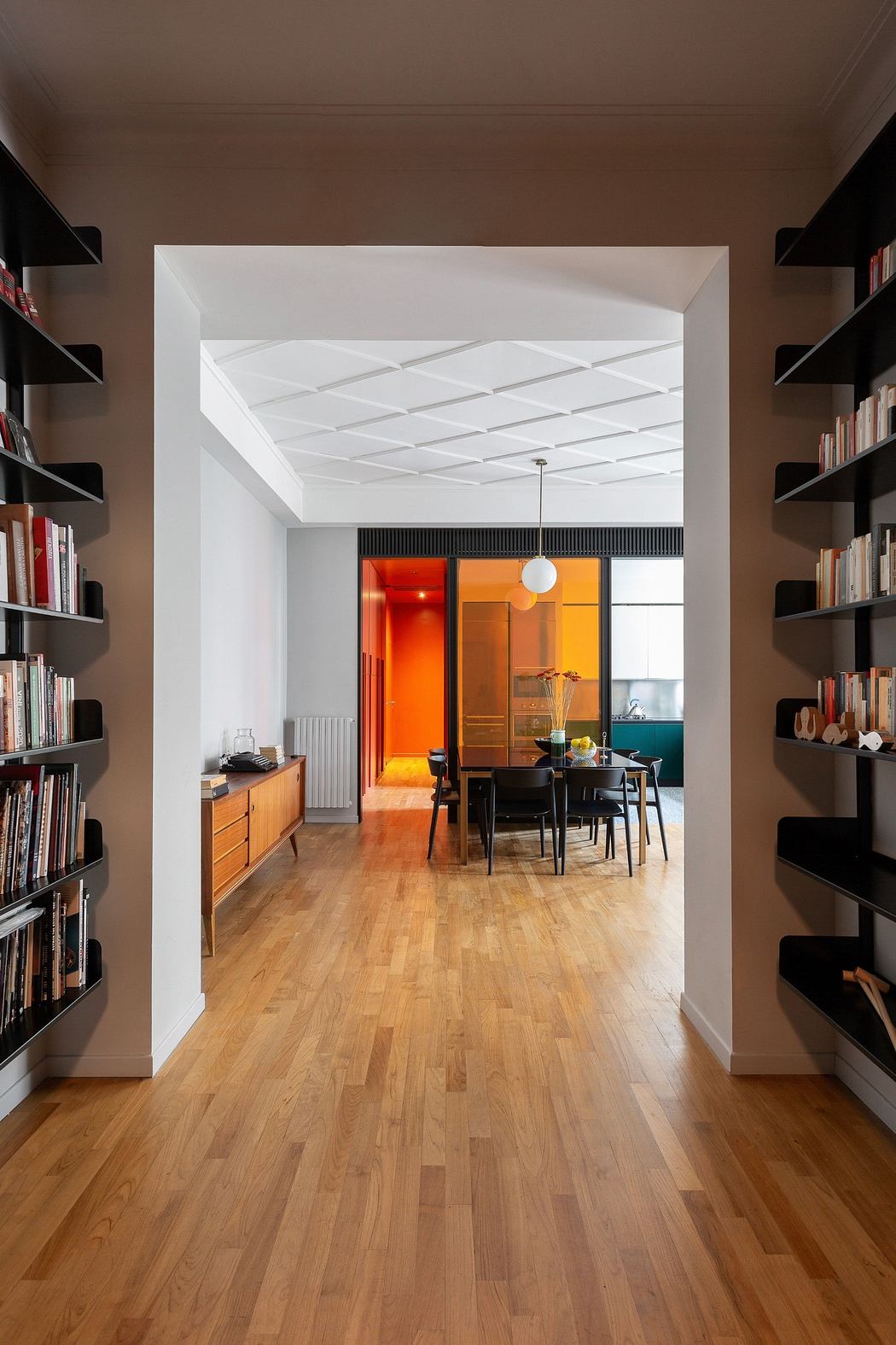 Modern hallway with bookshelves leading to a colorful dining area.