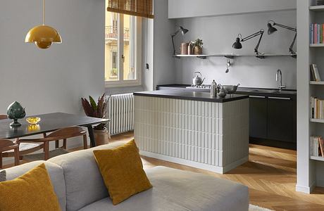 Modern living room with gray sofa, kitchen area, and yellow accents.