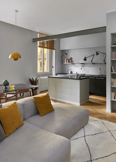 Modern living room with gray sofa, kitchen area, and yellow accents.