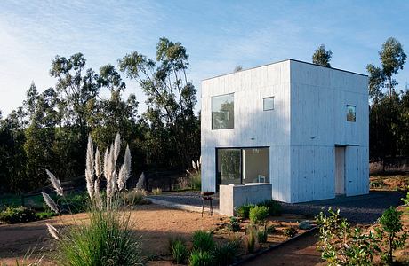 Modern two-story cubic house with large windows, surrounded by natural landscape.