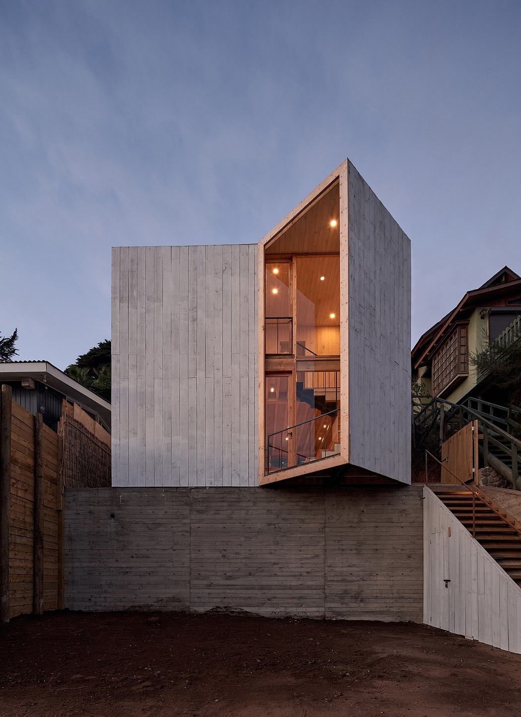 Contemporary vertical wooden house with large windows at dusk.