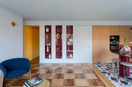 Modern interior with patterned floor, blue chair, and wood-panelled kitchen area