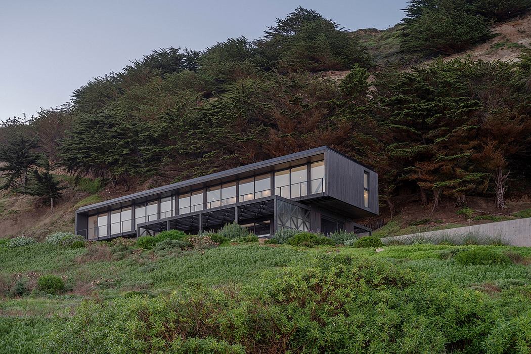 Modern cantilevered house on a hillside covered with shrubs.
