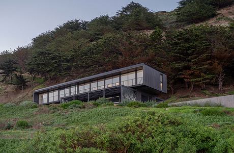 Modern cantilevered house on a hillside covered with shrubs.