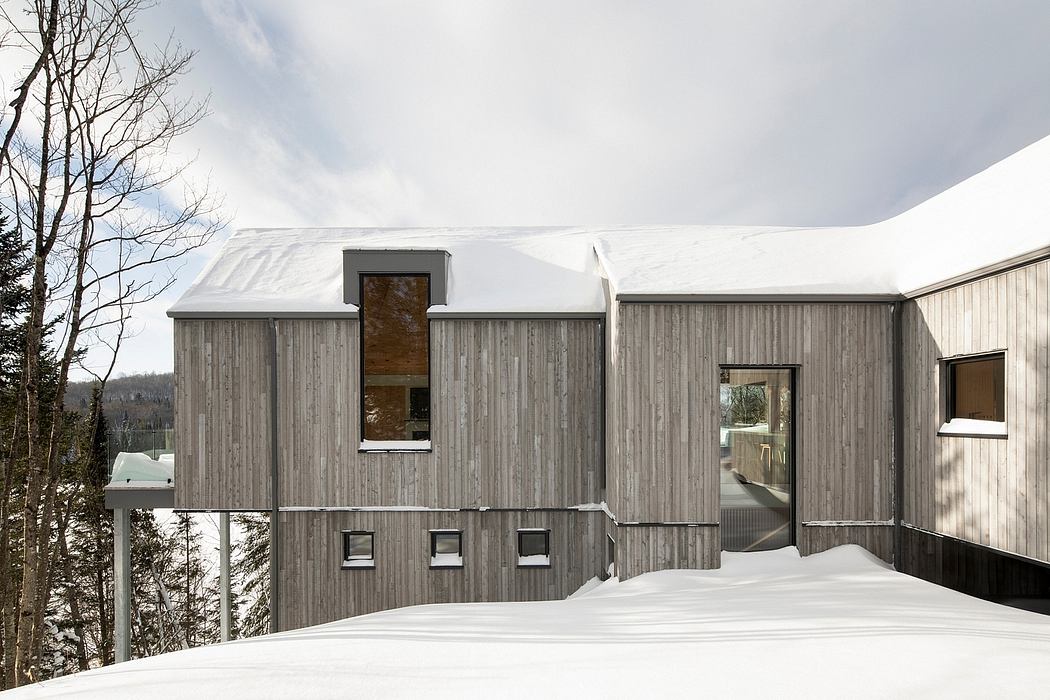 Contemporary wooden house with snow-covered roof nestled in a winter landscape.