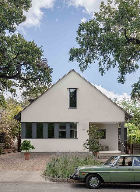 White modern house with gabled roof and vintage car parked in front.