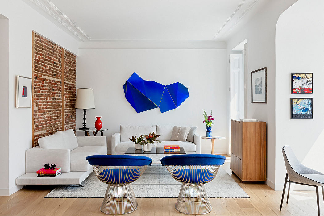 Modern living room with white sofa, blue chairs, and exposed brick wall.