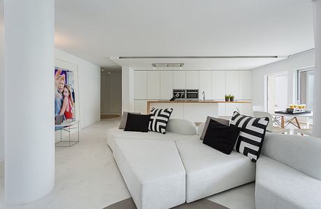 Contemporary interior with white sectional sofa, kitchenette, and colorful art.