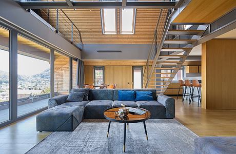 Modern living room with large windows, wooden ceiling, and grey sectional sofa.