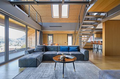 Modern living room with large windows, wooden ceiling, and grey sectional sofa.