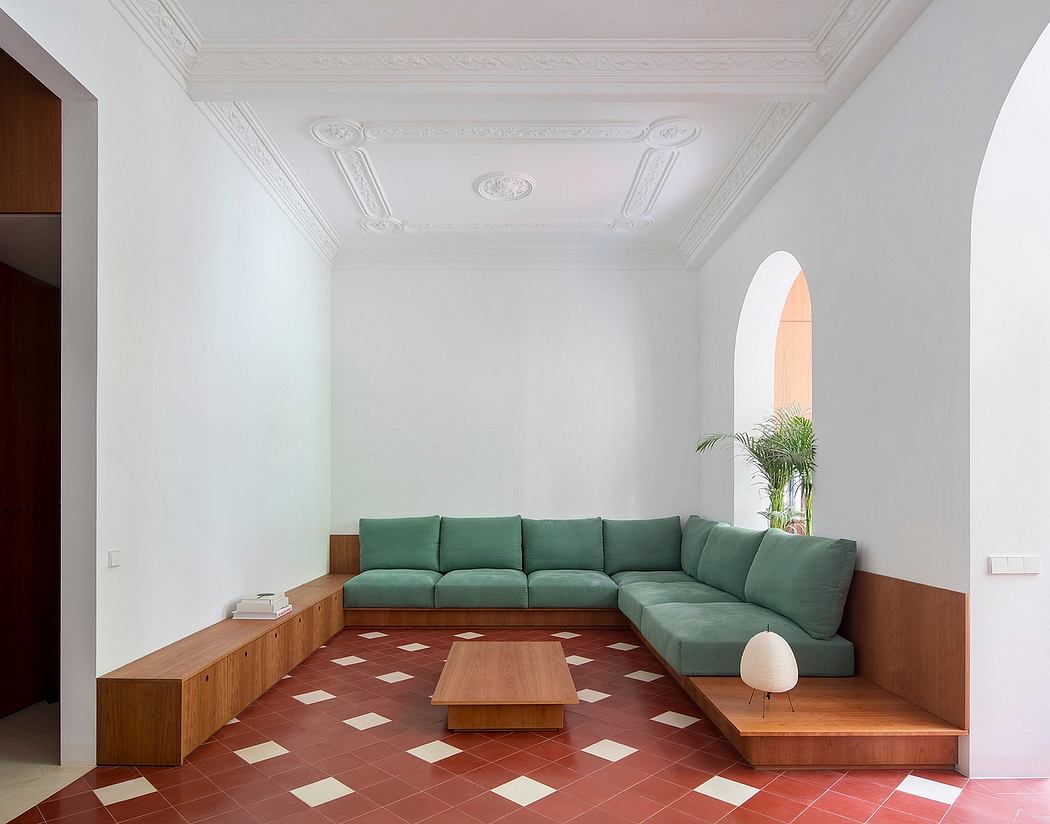 Minimalist living space with emerald green couch, terracotta tiled floor,