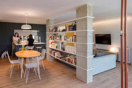 Contemporary living space with dining area, bookshelf partition, and lounge zone.